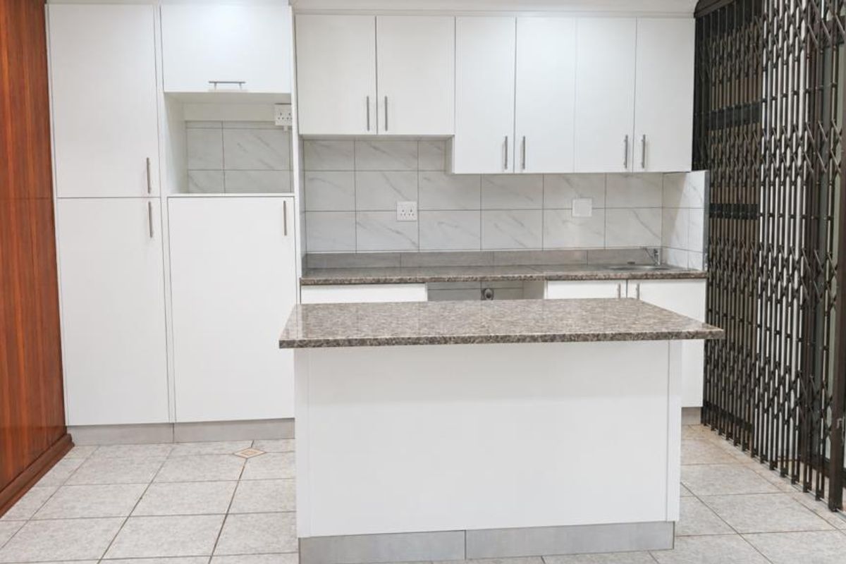 A clean, modern kitchen featuring white cabinetry, granite countertops, a central island, and tiled flooring, providing a functional and bright workspace.