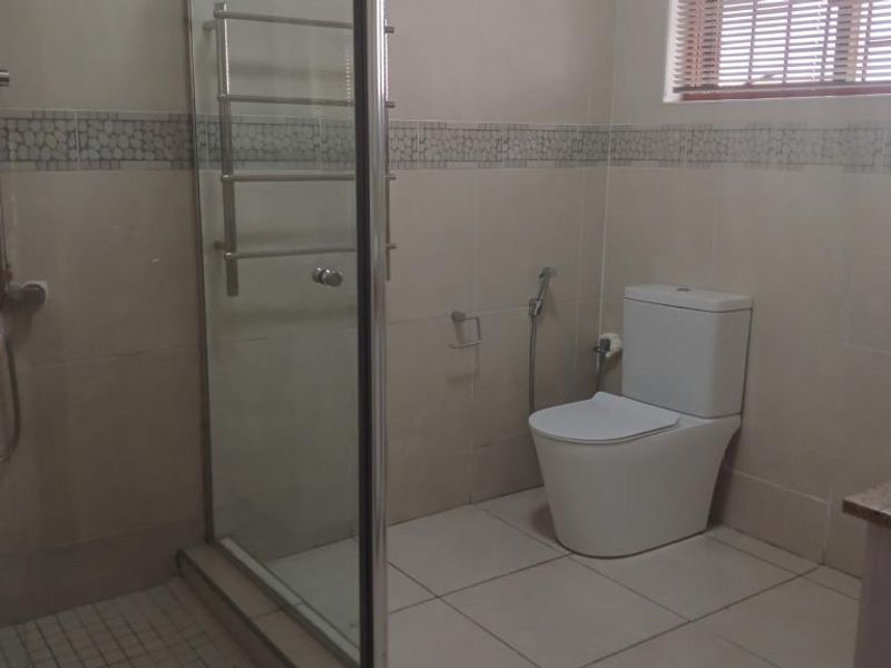 A functional bathroom featuring a glass-enclosed shower, modern toilet with bidet spray, heated towel rail, and a vessel sink on a vanity countertop.
