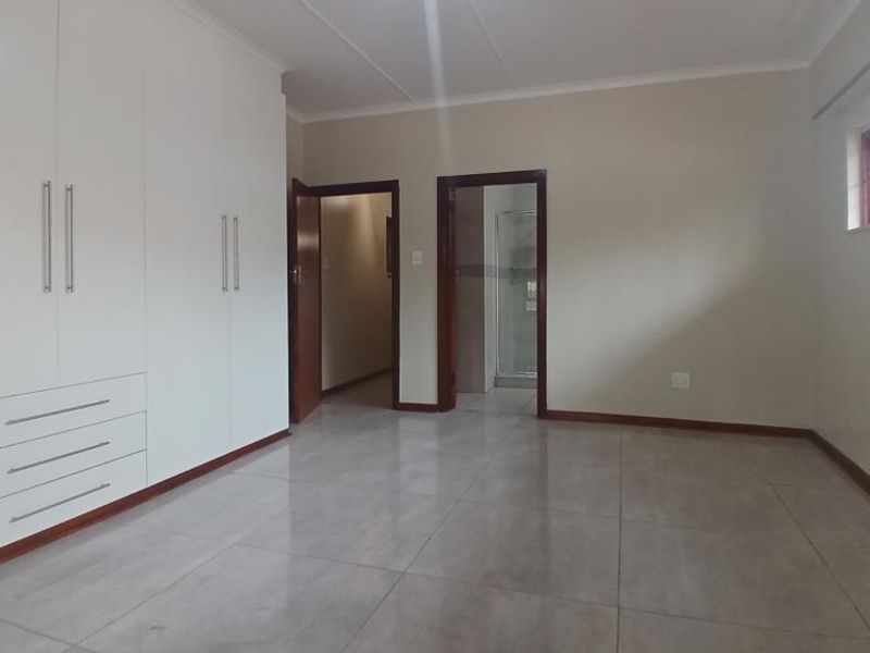 Spacious bedroom featuring neutral tiled flooring, extensive built-in cupboards, and direct access to an en-suite bathroom.