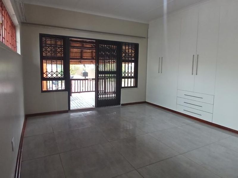 Spacious bedroom featuring large built-in cupboards, neutral tiled flooring, and direct access to an outdoor patio area through a secure sliding door.