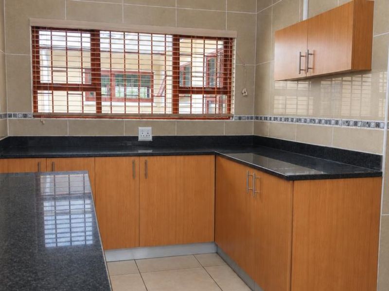A clean, functional kitchen featuring granite countertops, wood-finish cabinetry, and neutral wall tiling, offering a well-maintained space ready for personalization.