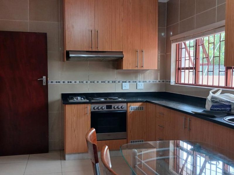 A functional kitchen featuring wood-finish cabinetry, granite countertops, a built-in oven with gas hob, and tiled finishes throughout.