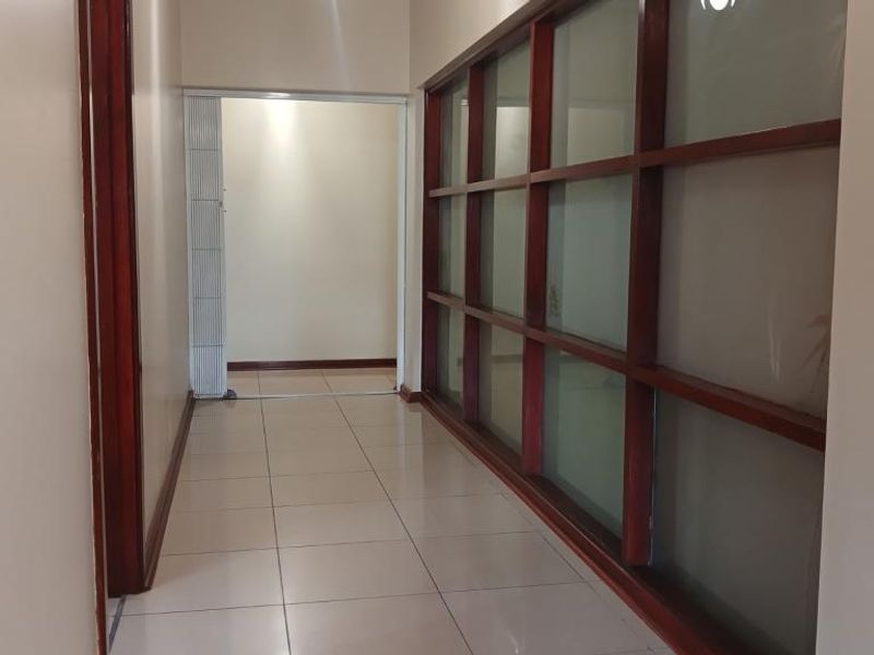 A clean, well-lit hallway featuring tiled flooring and a distinctive timber-framed glass partition wall, providing a bright and open transition between living spaces.