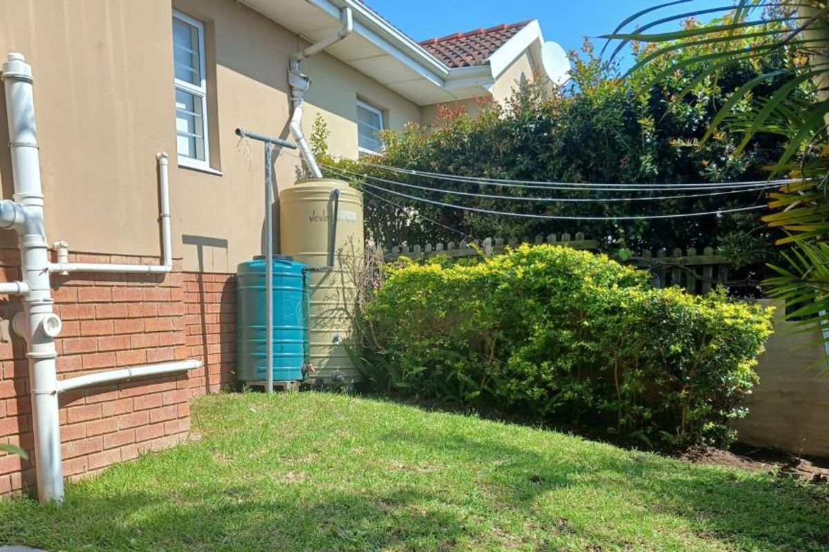 Rear garden area featuring a lawn, established shrubbery, external plumbing, and water storage tanks with a fixed washing line.