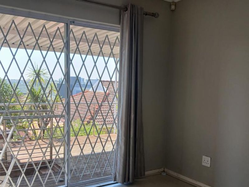 A bright, empty bedroom featuring a sliding glass door with a security gate, providing access to an outdoor patio area.