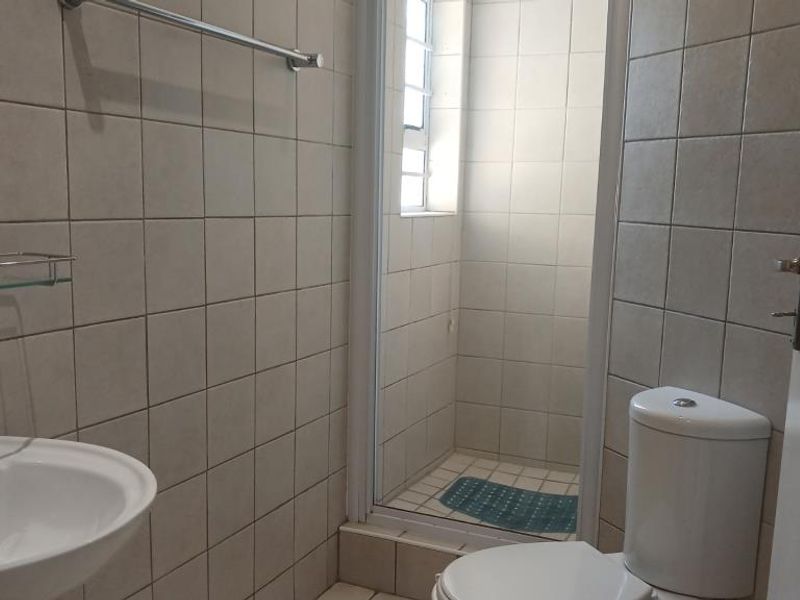 A functional bathroom featuring a pedestal basin, toilet, and a separate shower enclosure with neutral wall tiling.
