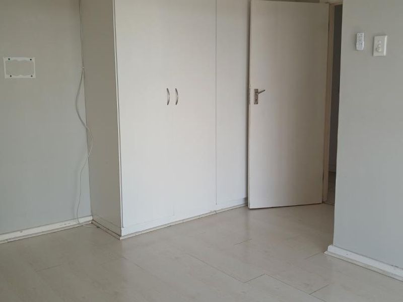 An empty bedroom featuring built-in cupboards and light-toned laminate flooring, offering a neutral canvas for personalization.