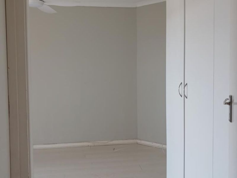 An empty bedroom featuring neutral wall tones, laminate flooring, and built-in cupboards, offering a clean and versatile space ready for personalization.