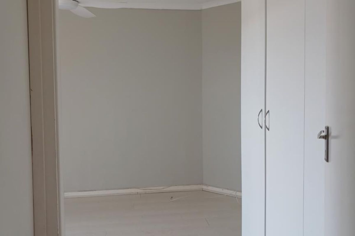 An empty bedroom featuring neutral wall tones, laminate flooring, and built-in cupboards, offering a clean and versatile space ready for personalization.
