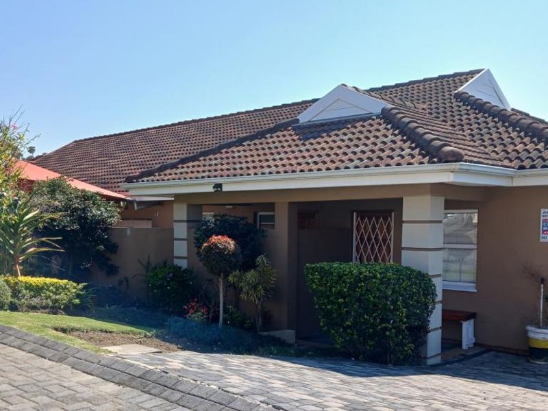 Front exterior view of a townhouse featuring a tiled roof, paved driveway, and secure entrance with security gate and bars.