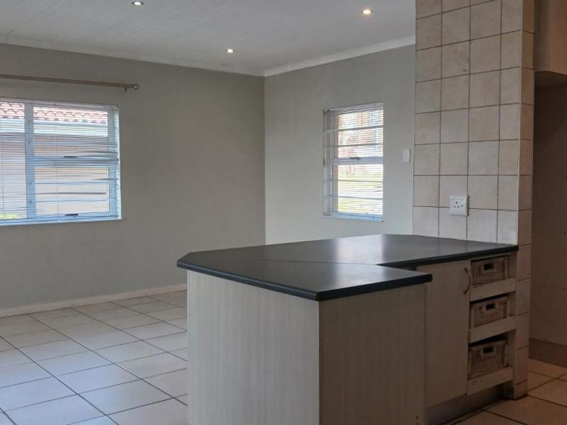 An open-plan living and kitchen area featuring tiled flooring, recessed lighting, and a functional kitchen island with built-in cabinetry.