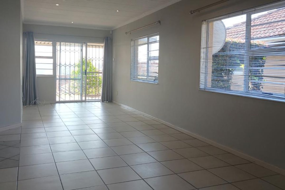 A spacious, empty living area featuring neutral tiled flooring, recessed lighting, and large windows with security gates and blinds, offering a bright, blank canvas.