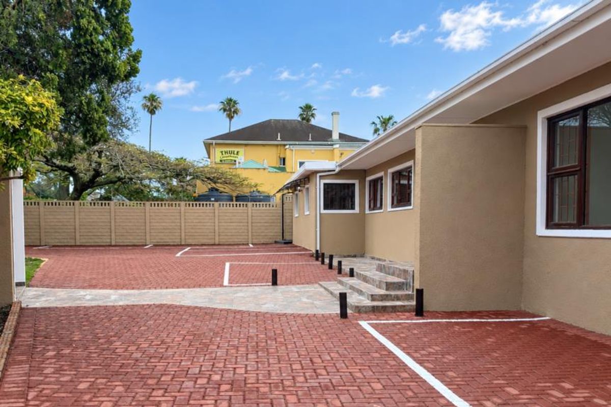 A well-maintained rear exterior area featuring a clean paved driveway, designated parking bays, and a secure precast boundary wall.