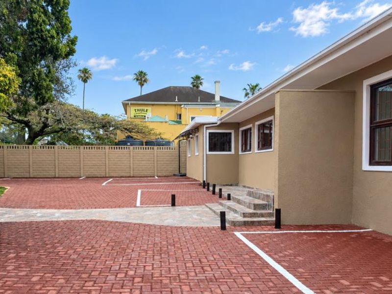 A well-maintained rear exterior area featuring a clean paved driveway, designated parking bays, and a secure precast boundary wall.