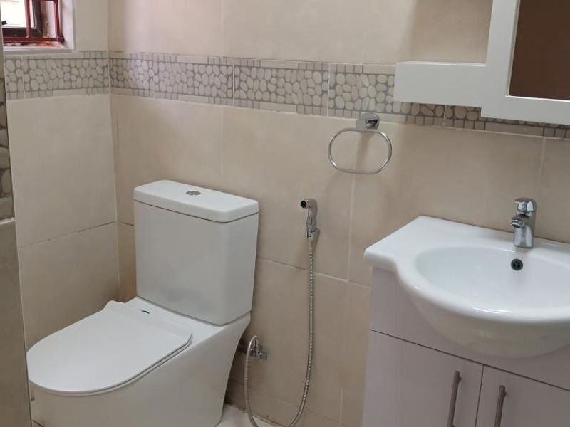A clean, functional bathroom featuring a modern toilet, a vanity cabinet with a washbasin, and decorative tiled walls.