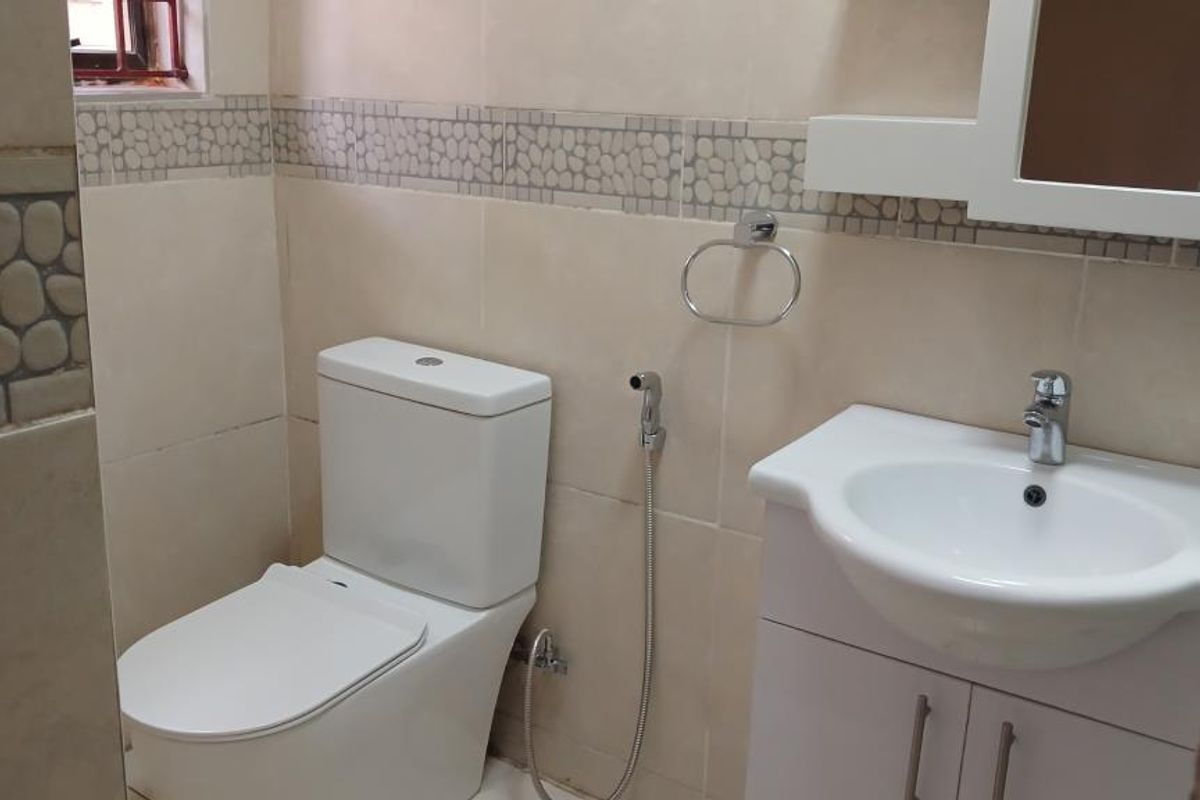 A clean, functional bathroom featuring a modern toilet, a vanity cabinet with a washbasin, and decorative tiled walls.