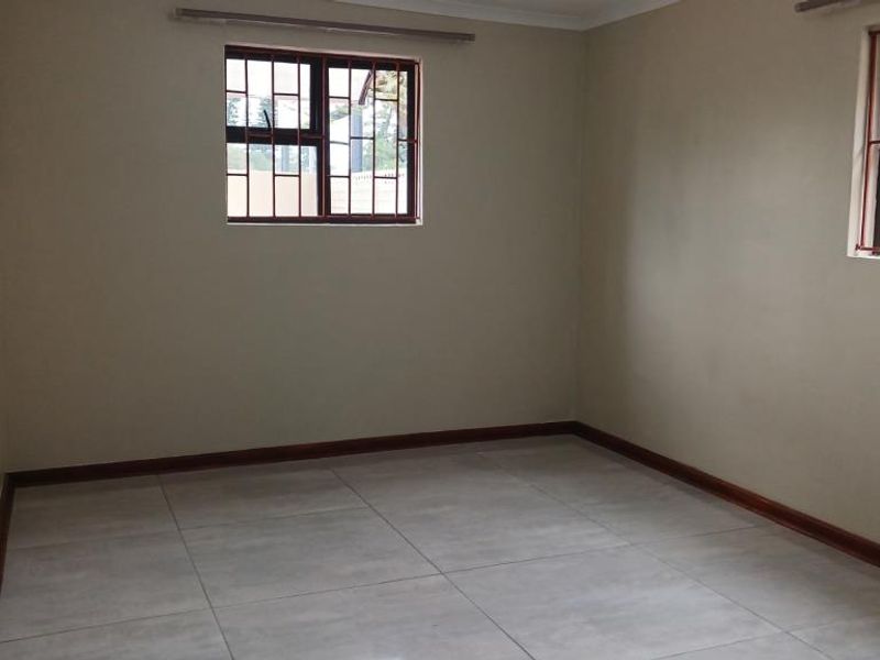 A clean, empty bedroom featuring neutral wall paint, large format floor tiles, and windows fitted with security burglar bars.