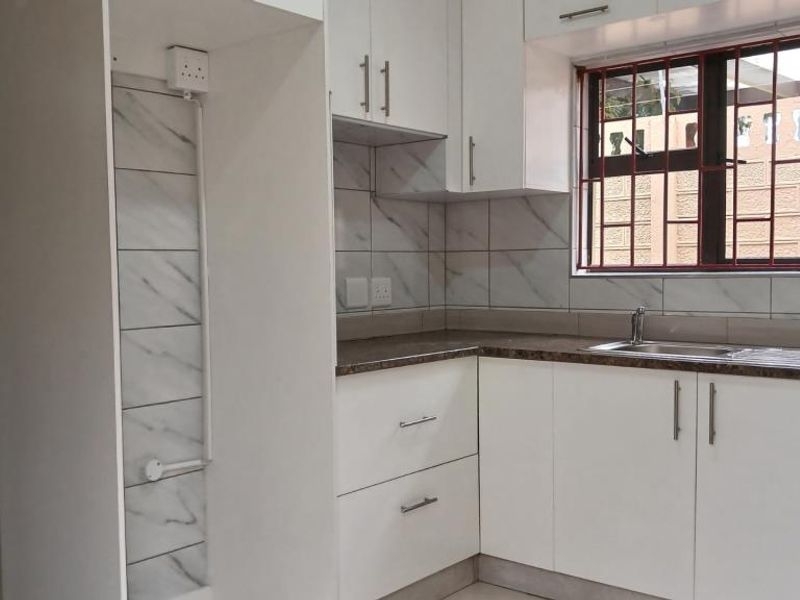 A clean, modern kitchen featuring white cabinetry, marble-look tiled backsplash, laminate countertops, and a stainless steel sink with security bars on the window.