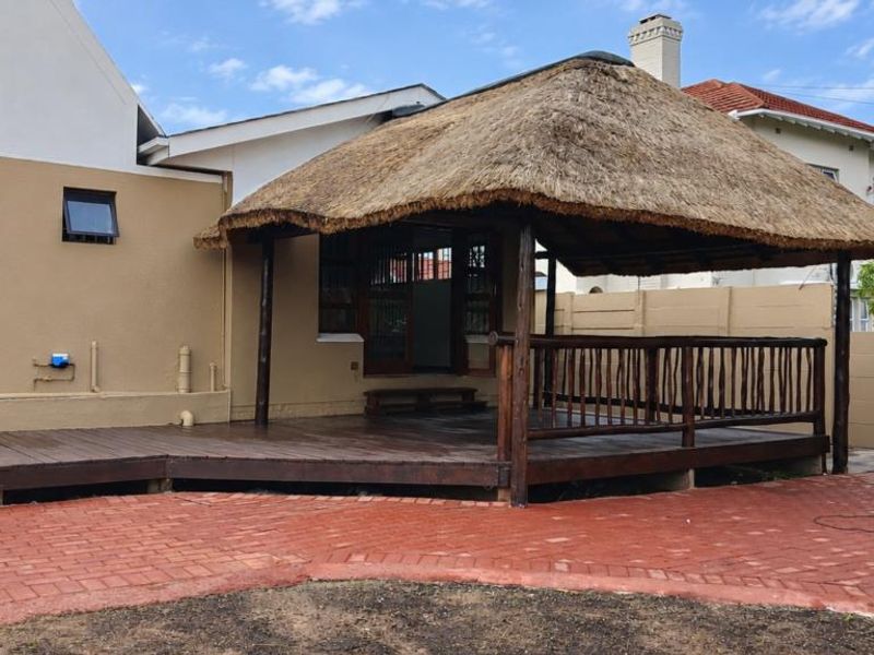 A covered outdoor patio area featuring a traditional thatched roof, timber decking, and surrounding brick paving in a private rear garden setting.