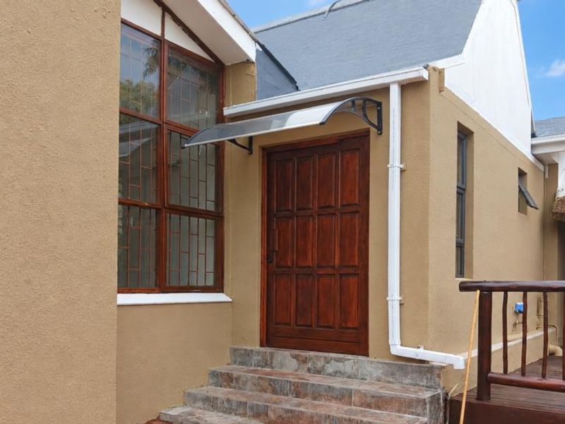 Exterior view of the apartment entrance featuring a wooden door, tiled steps, and a protective canopy, with a thatched roof structure visible nearby.