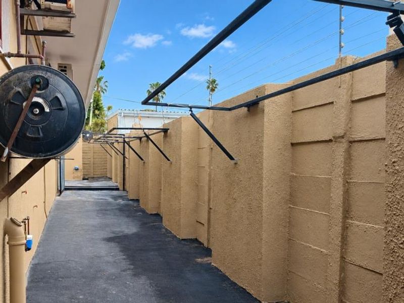 A side exterior walkway featuring a paved path, boundary wall with electric fencing, and an external geyser unit.
