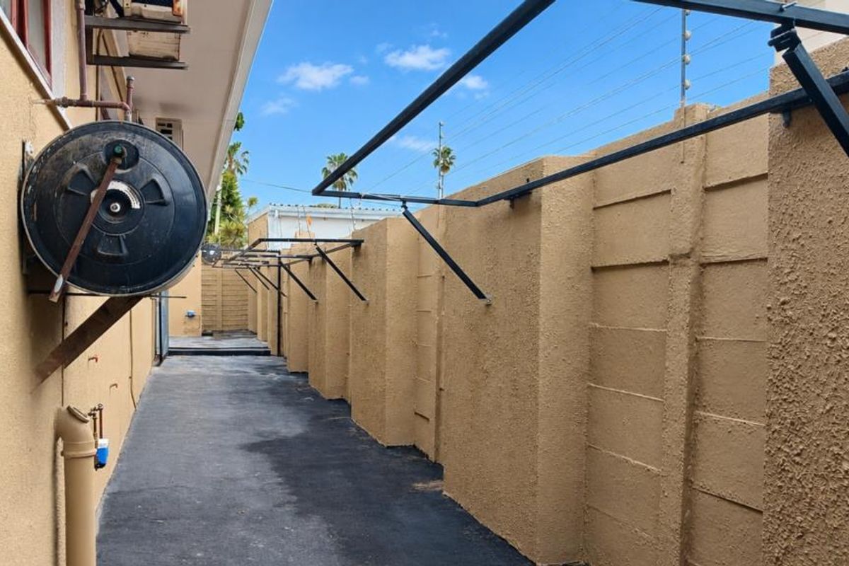 A side exterior walkway featuring a paved path, boundary wall with electric fencing, and an external geyser unit.