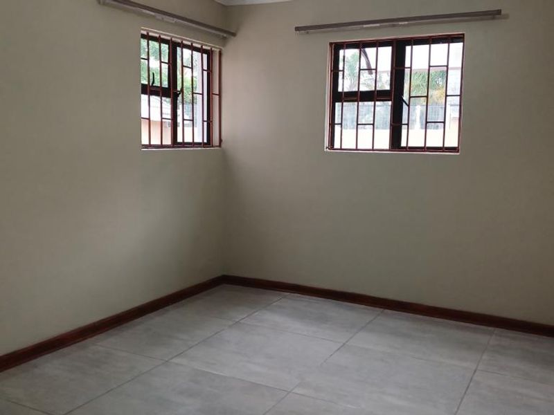 An empty bedroom featuring neutral wall paint, large format floor tiles, and windows fitted with security bars.