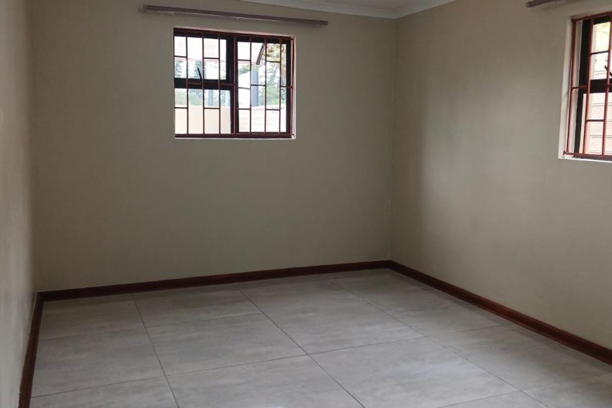 A clean, empty bedroom featuring neutral wall paint, large format floor tiles, and windows fitted with security burglar bars.