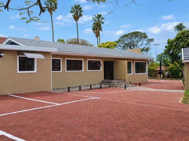 A well-maintained exterior view of the property featuring a spacious paved driveway, brick facade, and tiled roof with established landscaping.