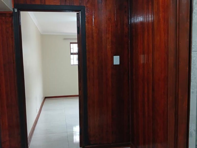 A hallway featuring dark timber wall paneling and light-colored tiled flooring, providing access to adjacent rooms.