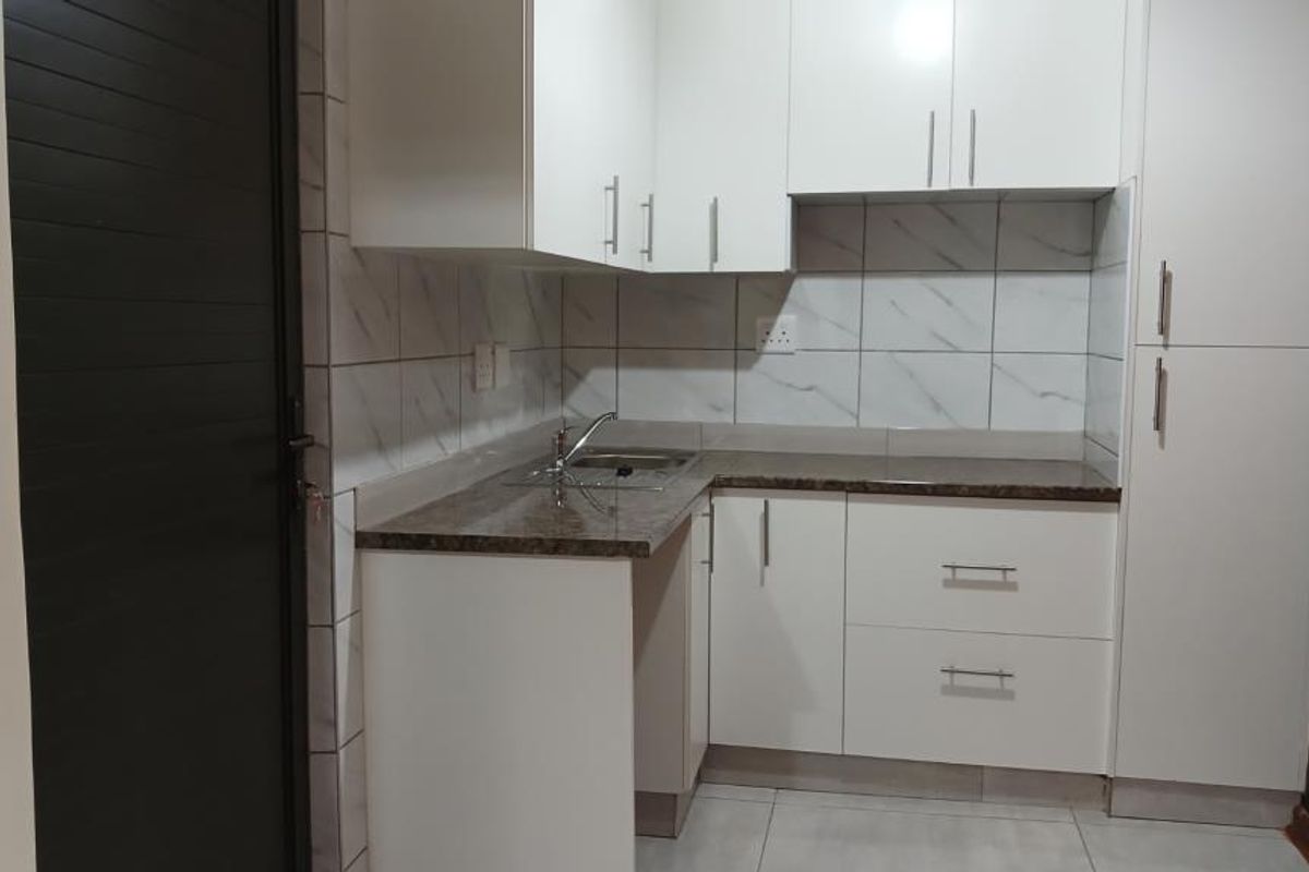 A compact, modern kitchen featuring white built-in cabinetry, a laminate countertop, stainless steel sink, and tiled backsplash.