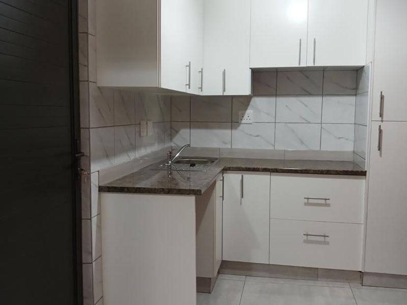 A compact, modern kitchen featuring white built-in cabinetry, a laminate countertop, stainless steel sink, and tiled backsplash.