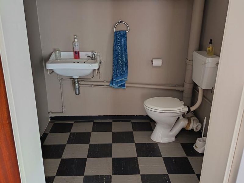 A compact bathroom featuring a wall-mounted basin, toilet, and overhead storage cabinetry with a checkered floor finish.