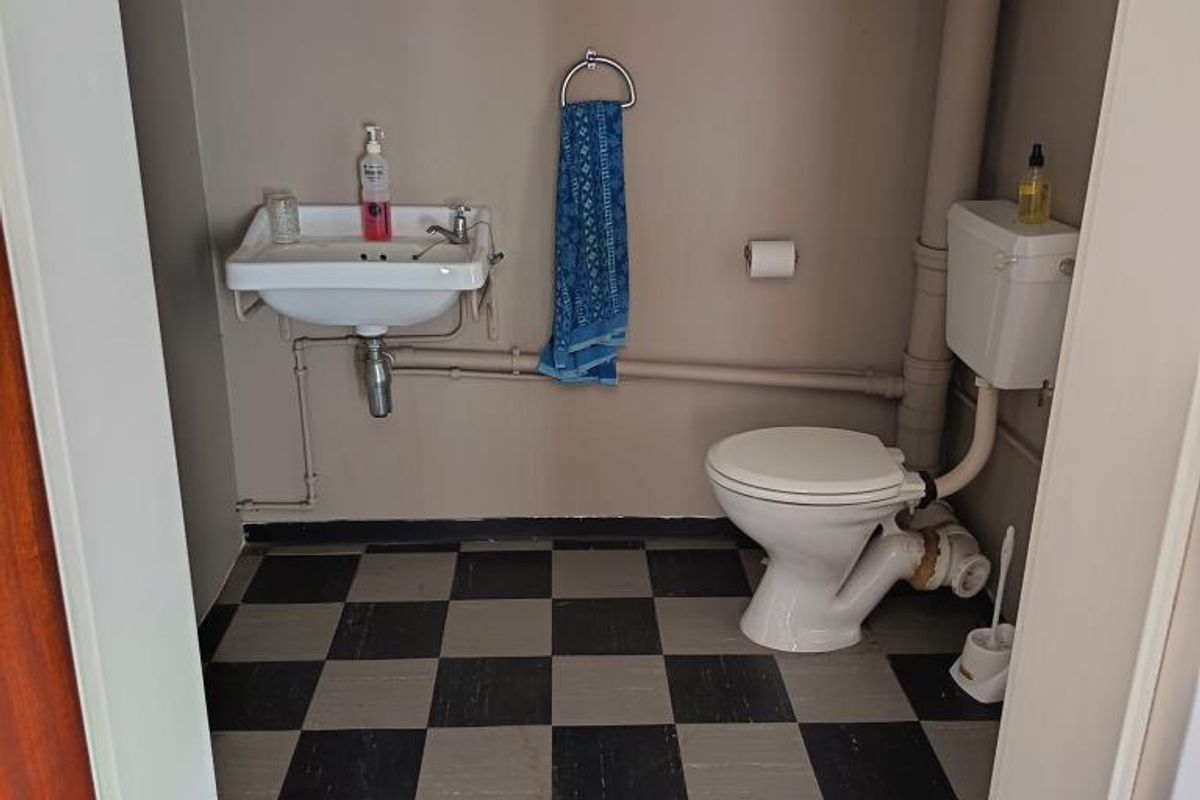 A compact bathroom featuring a wall-mounted basin, toilet, and overhead storage cabinetry with a checkered floor finish.