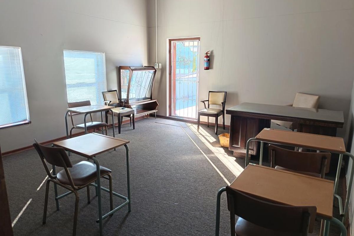 A functional office space featuring carpeted flooring, venetian blinds, and a wall-mounted fire extinguisher, suitable for a professional work environment.