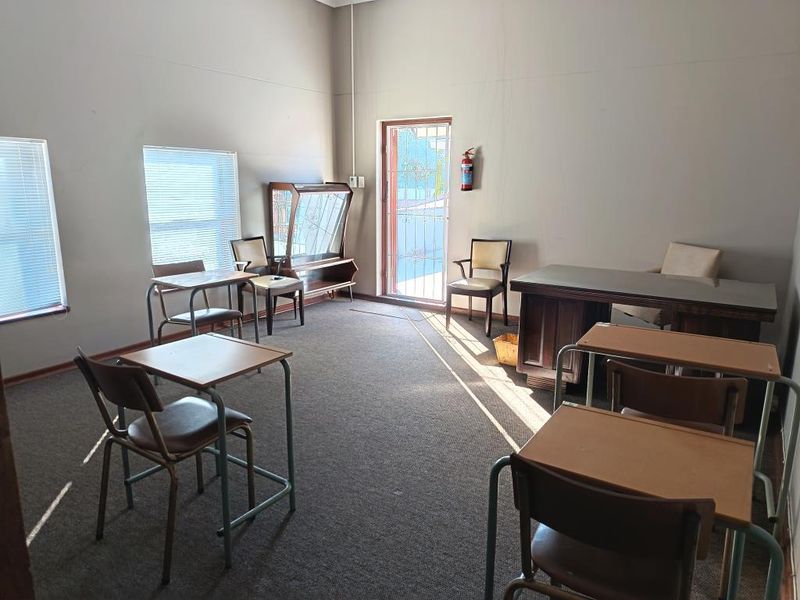 A functional office space featuring carpeted flooring, venetian blinds, and a wall-mounted fire extinguisher, suitable for a professional work environment.