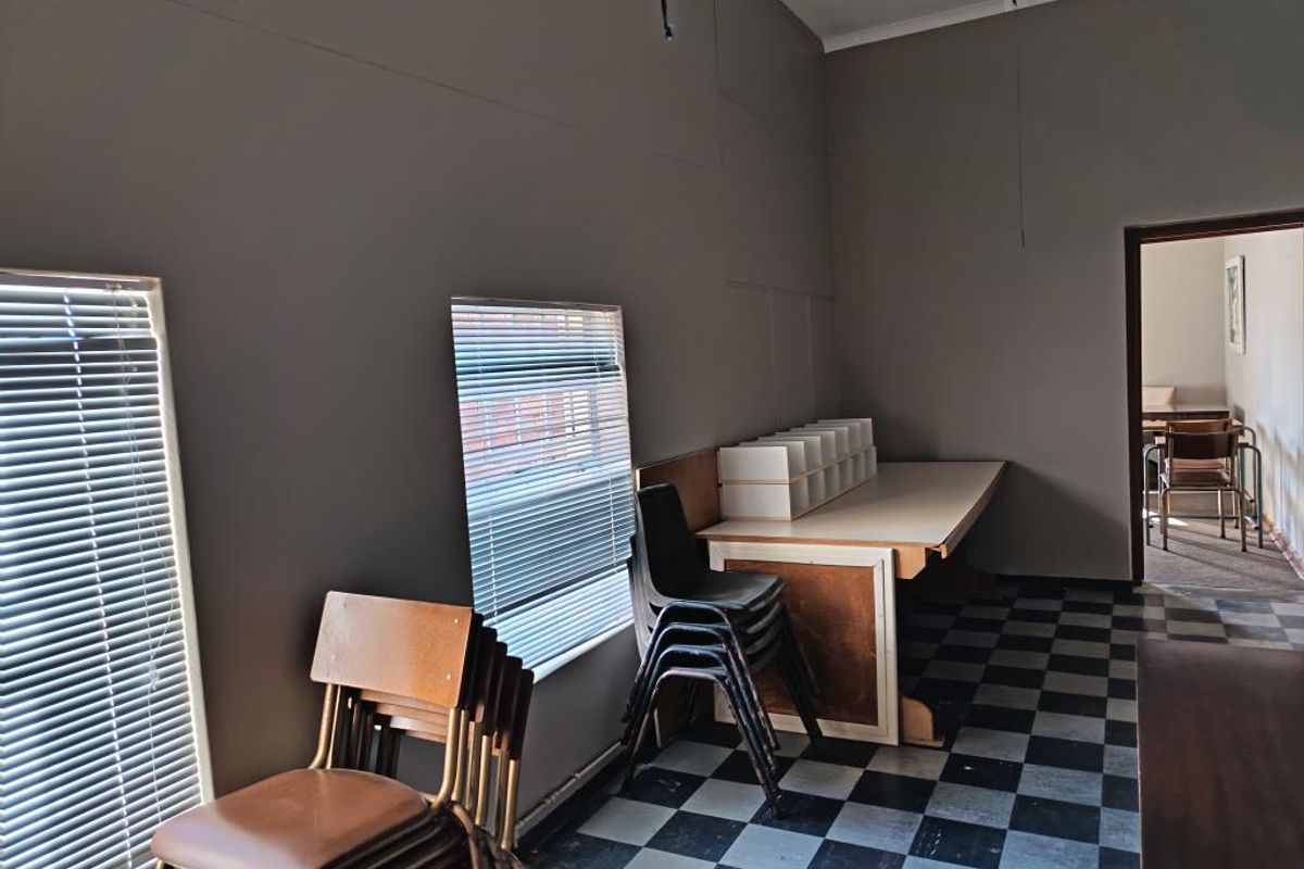 A functional office space featuring checkerboard flooring, venetian blinds, and a built-in desk, offering a practical layout for commercial use.