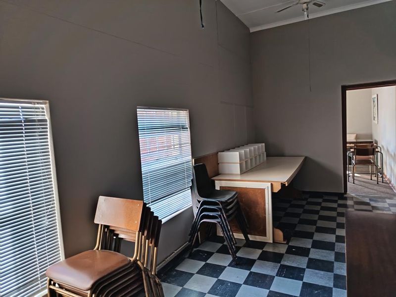 A functional office space featuring checkerboard flooring, venetian blinds, and a built-in desk, offering a practical layout for commercial use.