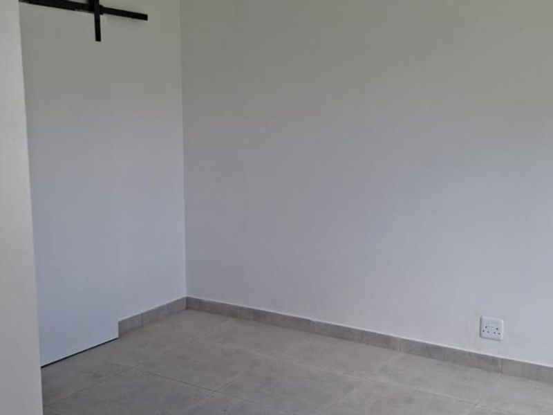 An empty bedroom featuring neutral tiled flooring, white walls, and a sliding door track, ready for personalization.
