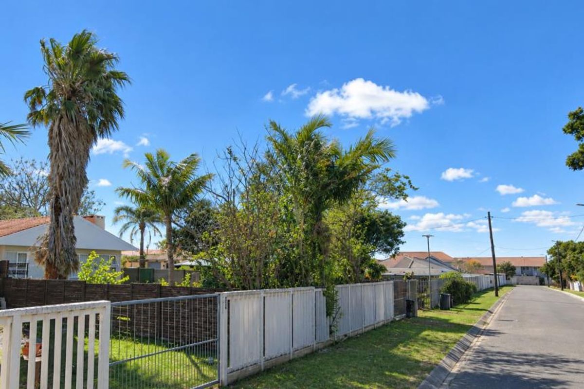 A street view showing the residential property boundary, perimeter fencing, and surrounding neighborhood infrastructure under a clear blue sky.