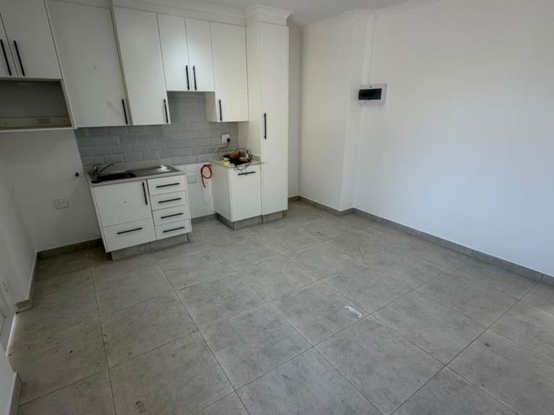An open-plan kitchen area featuring white cabinetry, subway tile backsplash, and neutral floor tiles. The space is vacant and ready for customization.