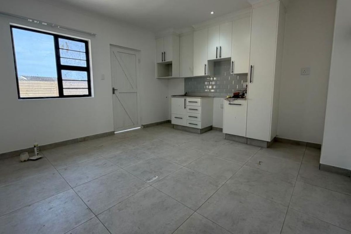 A clean, modern kitchen featuring white built-in cabinetry, a subway tile backsplash, and neutral tiled flooring in an open-plan layout.