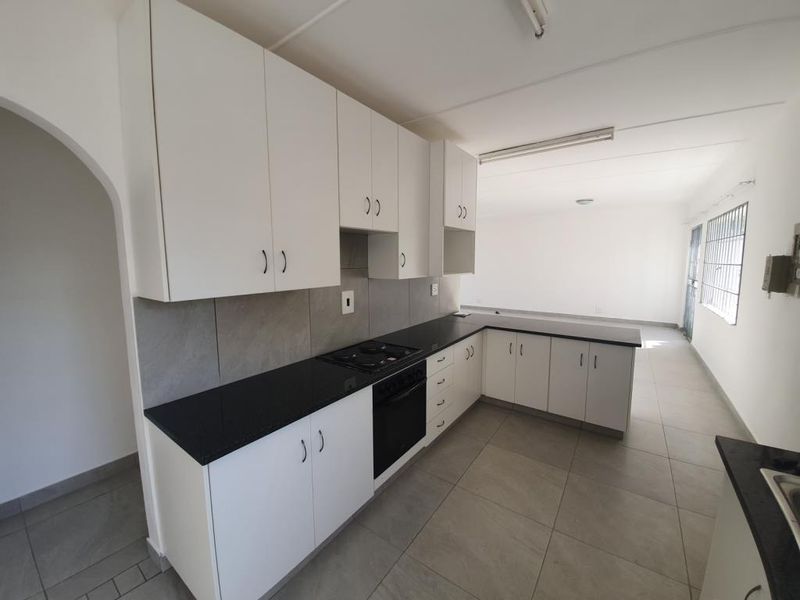 A clean, modern kitchen featuring white cabinetry, black stone countertops, a built-in oven and hob, and neutral floor tiles.