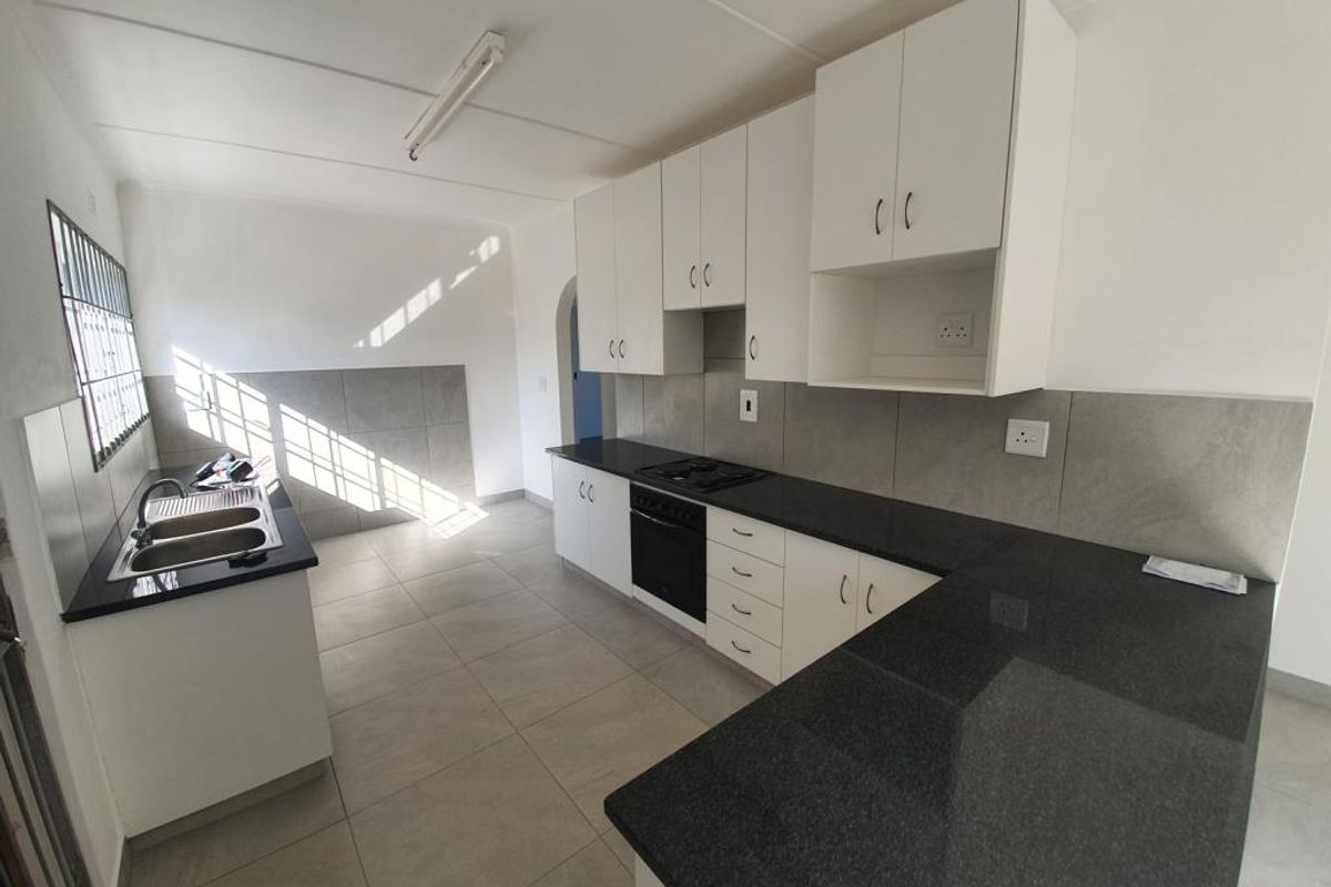 A clean, modern kitchen featuring white cabinetry, dark granite countertops, built-in oven and hob, and neutral tiled finishes throughout.
