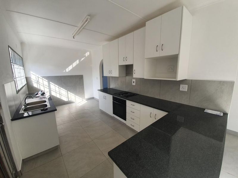 A clean, modern kitchen featuring white cabinetry, dark granite countertops, built-in oven and hob, and neutral tiled finishes throughout.
