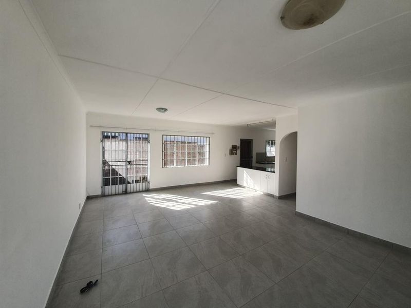 Spacious open-plan living area featuring tiled flooring, security bars on windows, and an integrated kitchen space with built-in cabinetry.