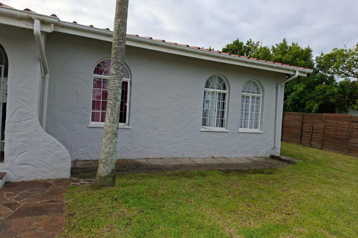 Rear exterior view of the property featuring arched windows, a tiled roof, stone paving, and a surrounding timber fence.