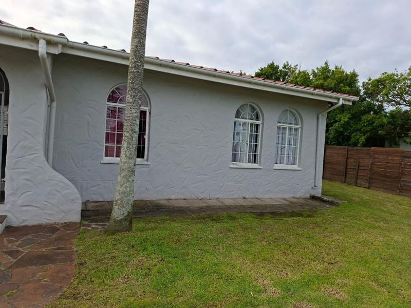 Rear exterior view of the property featuring arched windows, a tiled roof, stone paving, and a surrounding timber fence.