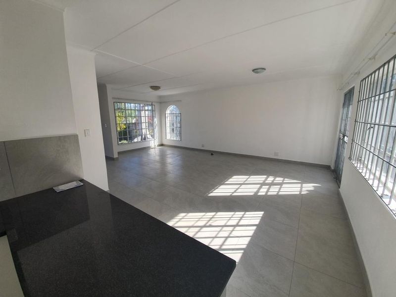 Spacious open-plan living and kitchen area featuring neutral tiled flooring, granite countertops, and large windows with security bars for added safety.
