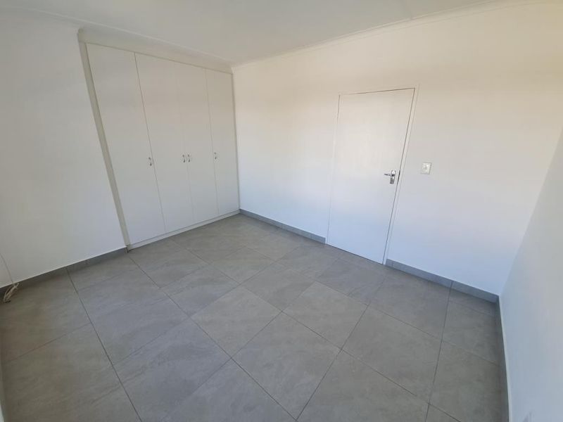 A clean, empty bedroom featuring neutral grey floor tiles and ample built-in cupboard storage, providing a versatile space ready for personalization.